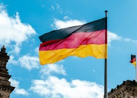 Vibrant German flag waving on a flagpole against a bright blue sky with clouds.