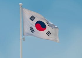 South Korean national flag fluttering on a flagpole against a clear blue sky in Seoul.