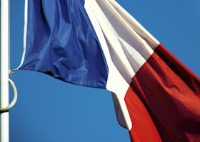 A close-up of the French national flag waving against a clear blue sky in Paris, France.