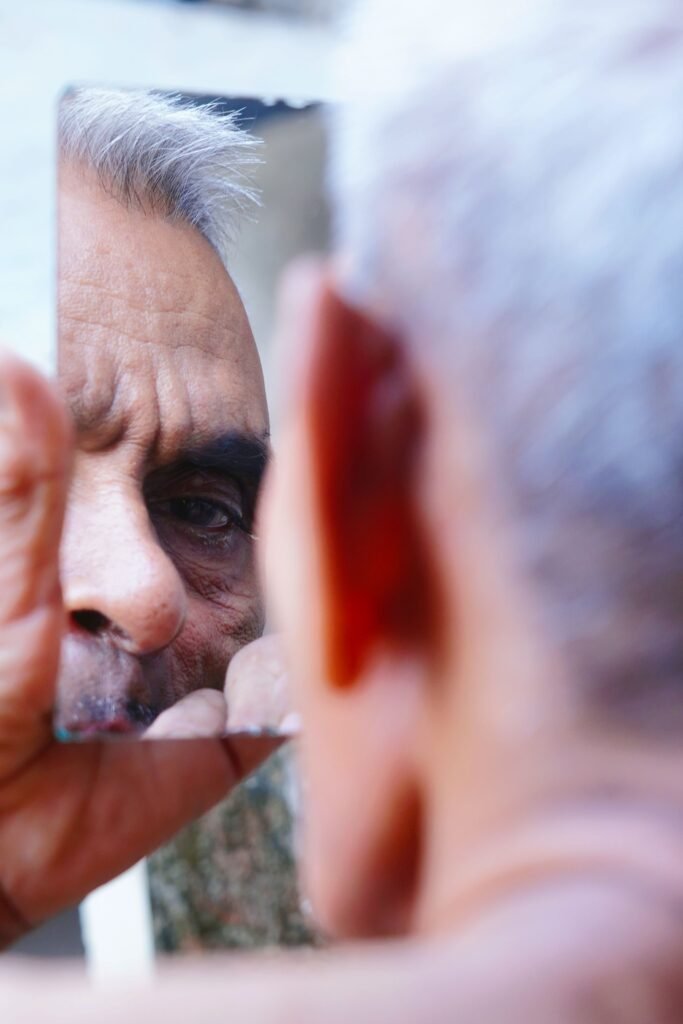 Close-up of an elderly man looking at his reflection in a handheld mirror.